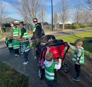 Children on a nature walk in hi vis vests with educators in Romsey