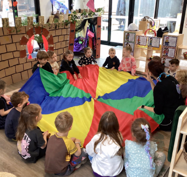 Children playing with a rainbow parachute at Romsey Early Learning